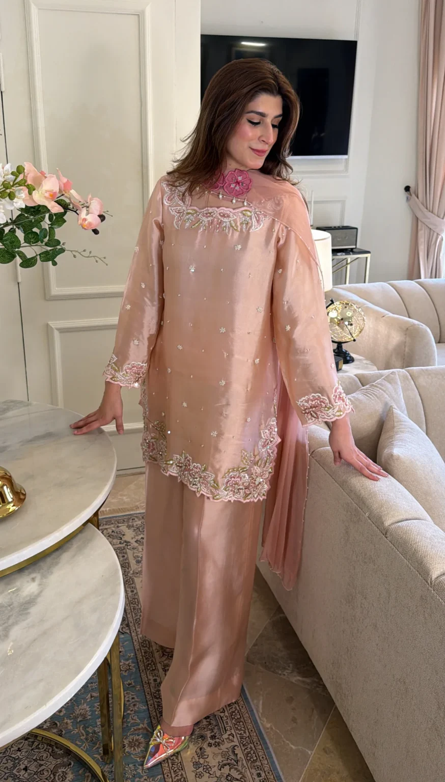 Soft pink three-piece: a long-sleeved silk shirt with small clusters of pearl-like beads and ivory, pink and olive embroidery along a scalloped neckline, cuffs and hem, worn with wide full-length trousers and a sheer dupatta edged in pearl-like beads
