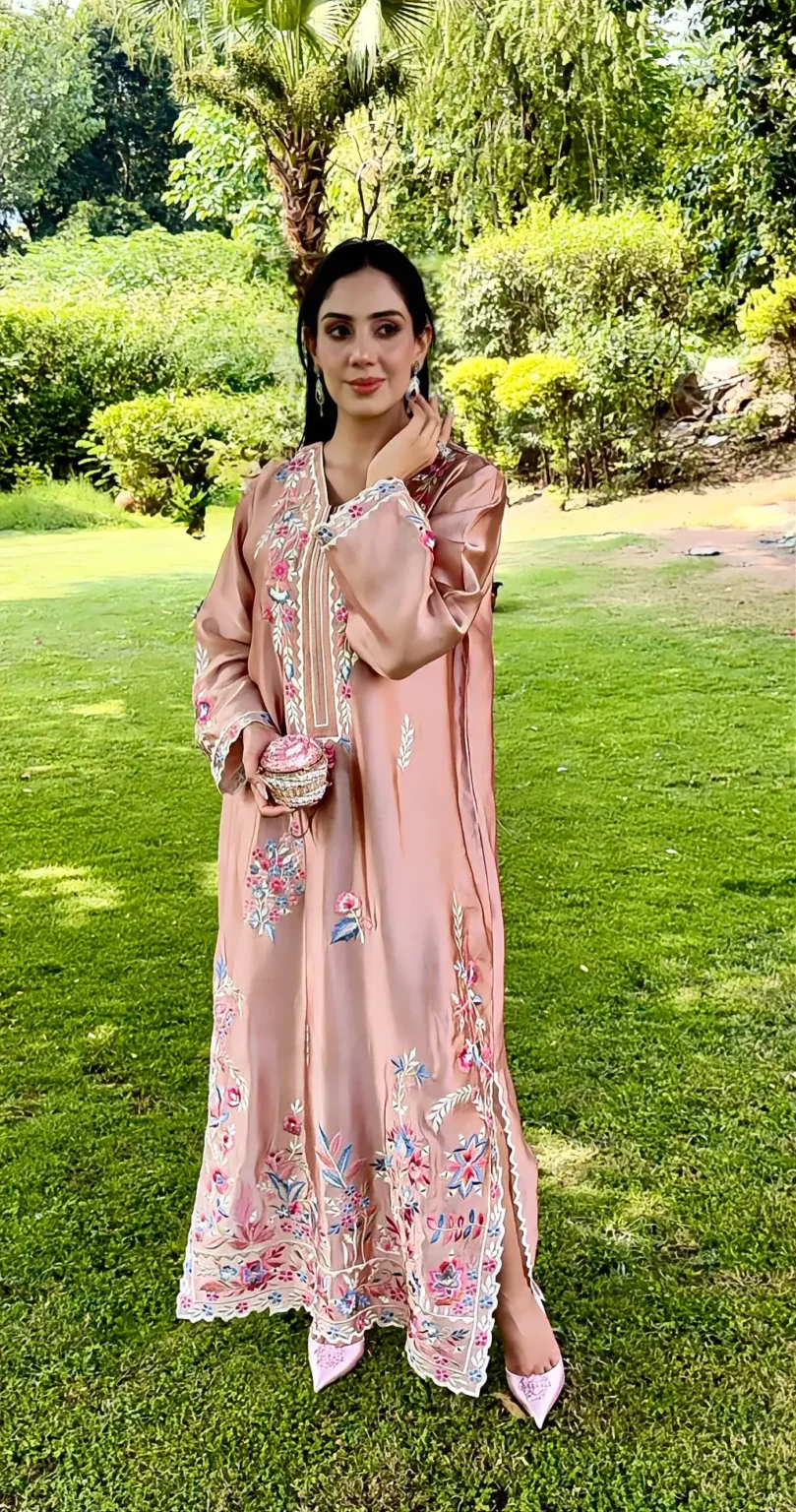 Front view of the tea pink silk kaftan, with a narrow band of ivory lines down the front, fuchsia and powder-blue flowers along the neckline, and a scalloped floral border at the hem