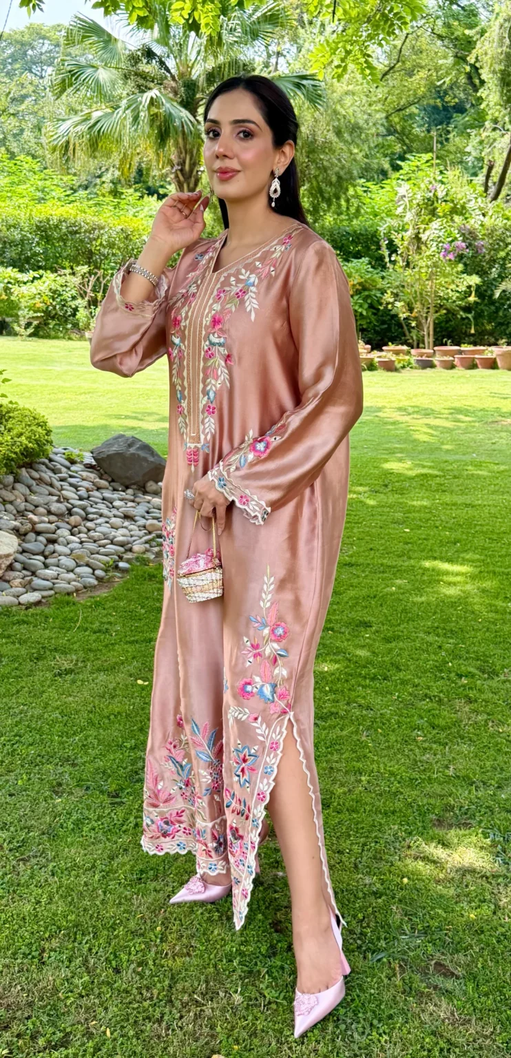 Long tea pink silk kaftan with a V neck, full sleeves ending in ivory cuffs, pink and blue flowers down the front, a deep floral border at the hem, and a side slit edged in ivory scallops