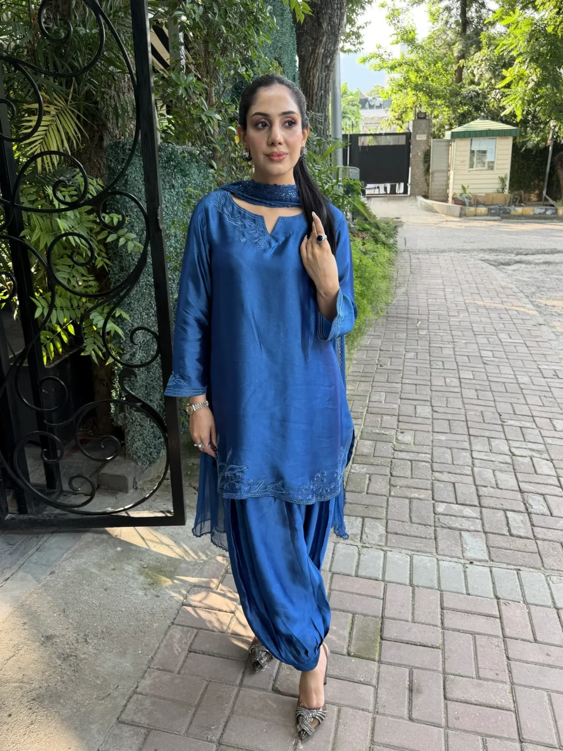 Short sapphire blue silk shirt with a notched round neck and pale blue leaf and flower embroidery at the neck and hem, worn with a draped shalwar gathered at the ankle and a blue dupatta wrapped at the throat