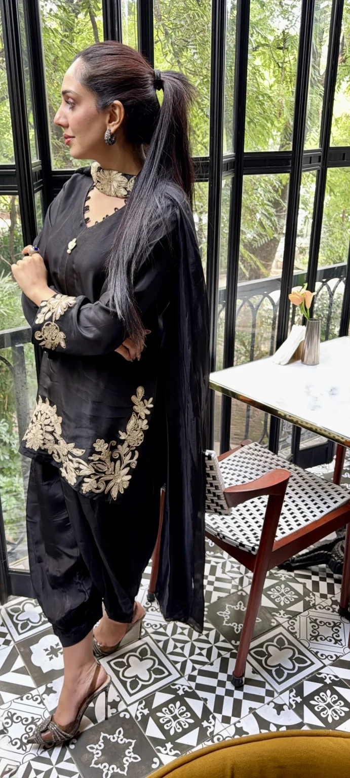 Side view of the black shisha silk shirt showing the champagne choker band, an embroidered cuff, hem flowers climbing toward the hip and the sheer black dupatta hanging down the back
